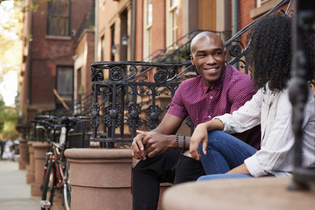 Couple Sit And Talk On Stoop Of Brownstone In New York Cityの写真素材