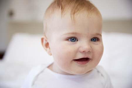 Close Up Of Happy Baby Boy Sitting On Parents Bedの写真素材