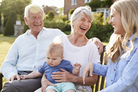 Grandparents Sit Outdoors With Baby Grandson And Adult Daughter