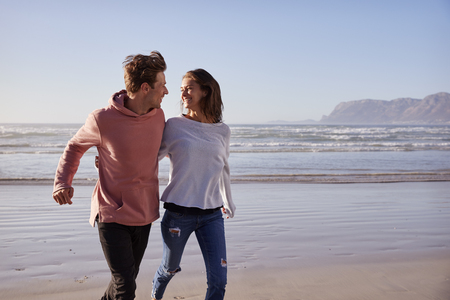 Couple Having Fun Running Along Winter Beach Togetherの写真素材
