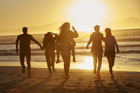 Silhouette Of Friends Having Fun Running Along Winter Beachの写真素材