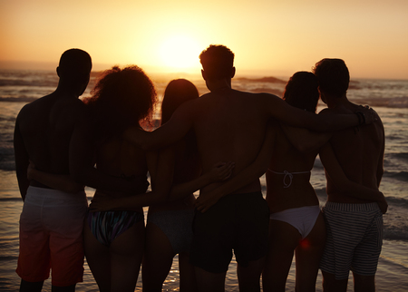 Silhouette Of Friends On Beach Vacation Watching Sunset Over Seaの写真素材