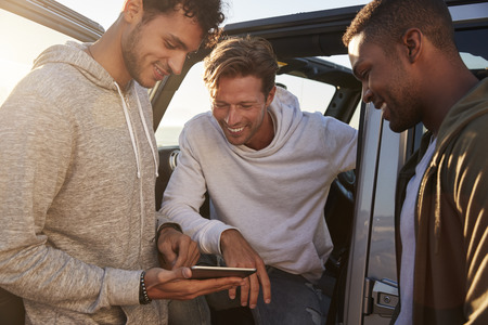 Male friends planning road trip route with tablet computerの写真素材