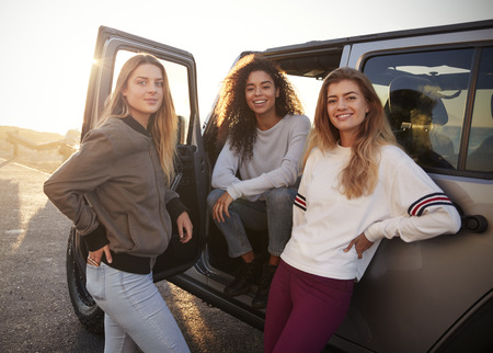 Three female friends on road trip looking at camera from carの写真素材