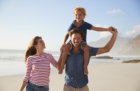 Portrait Of Parents Carrying Son On Shoulders On Beach Vacation