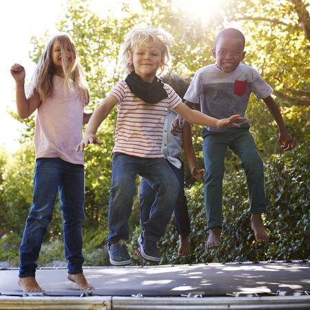 Four kids having fun together on a trampoline in the gardenの写真素材