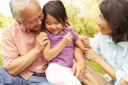 Grandparents Cuddling Granddaughter In Park