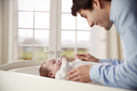 Father Playing With Newborn Baby Lying On Changing Table