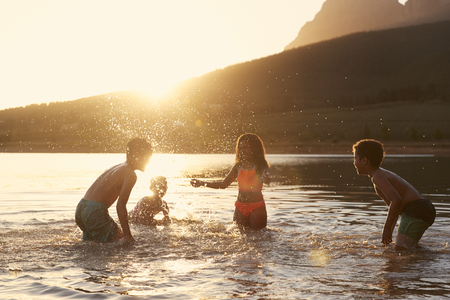 Children With Friends Enjoying Evening Swim In Countryside Lakeの写真素材