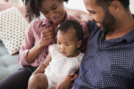 Family With Baby Daughter Sitting On Sofa At Home Together