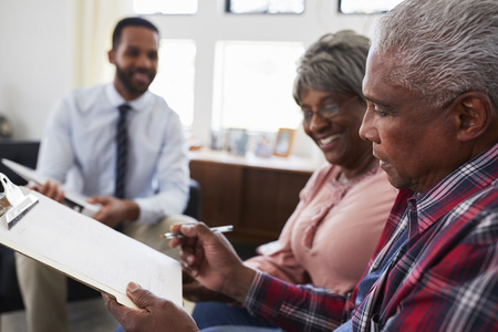 Senior Couple Meeting With Male Financial Advisor At Home And Signing Documentの写真素材