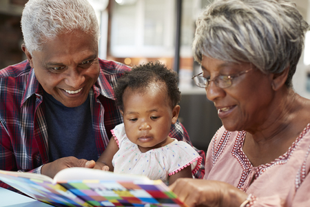 Grandparents Reading Book With Baby Granddaughter At Homeの写真素材