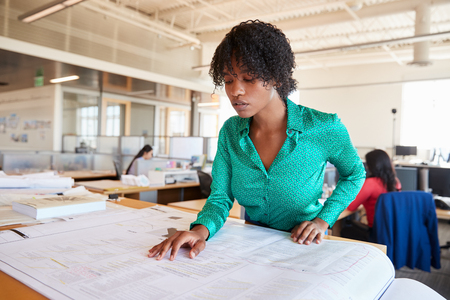Black female architect studying plans in open plan officeの写真素材