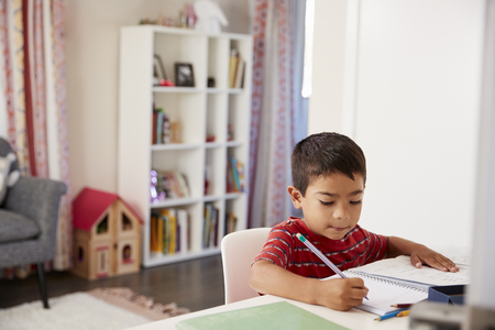 Young Boy Sitting At Desk In Bedroom Doing Homeworkの写真素材