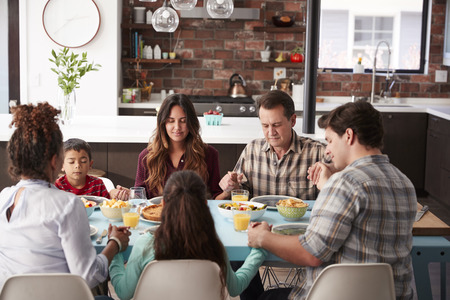Multi Generation Family Praying Before Meal Around Table At Homeの写真素材