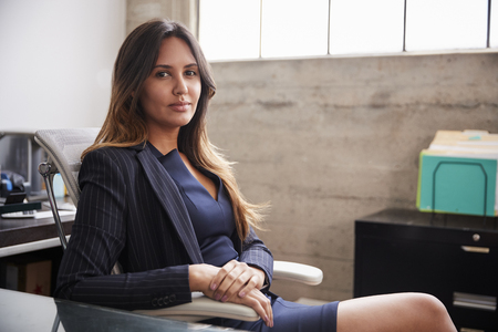 Mixed race woman sitting at desk in office turning to cameraの写真素材