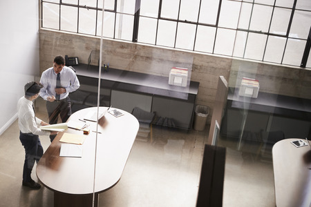 Two businessmen stand talking over paperwork in an officeの写真素材