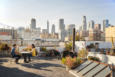 Couple Drinking Wine And Making Toast On Rooftop Terrace With City Skyline In Backgroundの写真素材