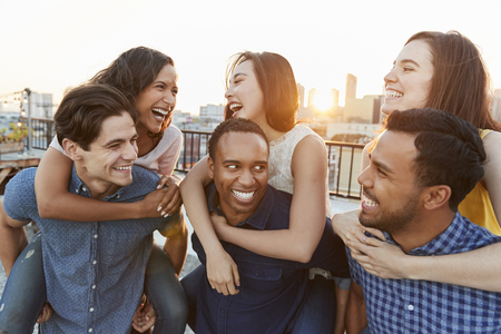 Men Giving Women Piggybacks On Roof Terrace With City Skyline In Backgroundの写真素材