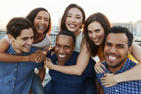 Portrait Of Men Giving Women Piggybacks On Roof Terrace With City Skyline In Backgroundの写真素材