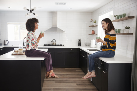 Two Female Friends Meeting For Coffee At Home Sitting On Kitchen Islandの写真素材