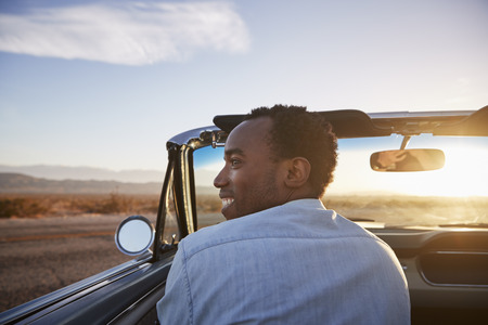 Rear View Of Man On Road Trip Driving Classic Convertible Car Towards Sunsetの写真素材