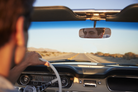 Rear View Of Man On Road Trip Driving Classic Convertible Car Towards Sunsetの写真素材