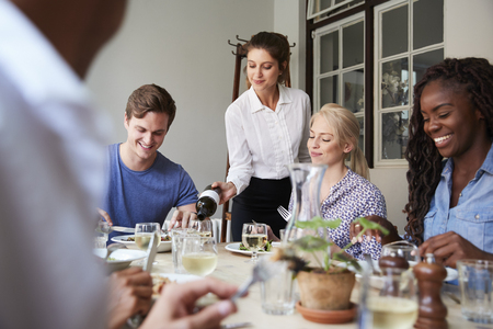 Waitress Pouring Wine For Group Of Friends Enjoying Meal In Restaurant Togetherの写真素材