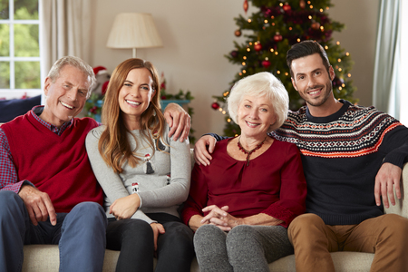 Portrait Of Senior Parents With Adult Offspring Wearing Festive Jumpers Sitting On Sofa In Lounge At Home On Christmas Dayの写真素材