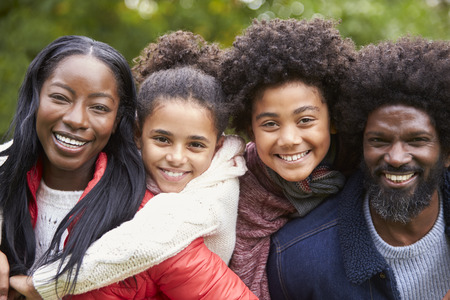Mixed race family smiling to camera, parents piggybacking kids in the park, close upの写真素材