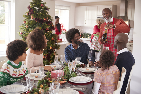 Black grandfather opening champagne for his multi generation family, gathered in the dining room for Christmas dinnerの写真素材