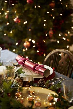 Christmas table setting a with Christmas cracker arranged on a plate and table decorations, a Christmas tree in the backgroundの写真素材