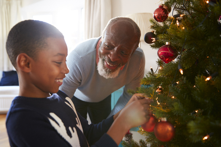 Grandfather And Grandson Hanging Decorations On Christmas Tree At Home Togetherの写真素材