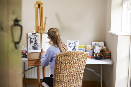 Female Teenage Artist Sitting At Easel Drawing Picture Of Dog From Photograph In Charcoalの写真素材