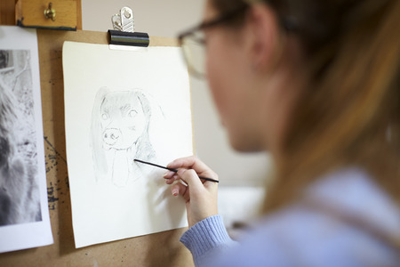 Close Up Of Female Teenage Artist Sitting At Easel Drawing Picture Of Dog From Photograph In...