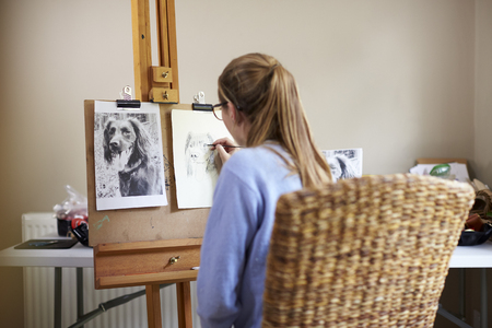 Rear View Of Female Teenage Artist Sitting At Easel Drawing Picture Of Dog From Photograph In Charcoalの写真素材