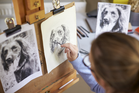 Rear View Of Female Teenage Artist Sitting At Easel Drawing Picture Of Dog From Photograph In Charcoalの写真素材