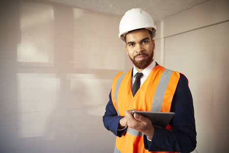 Portrait Of Surveyor In Hard Hat And High Visibility Jacket With Digital Tablet Carrying Out House...