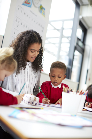 Two infant school kids and their female teacher sitting at table in a classroom drawing, low angleの写真素材