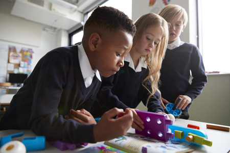 Close up of three primary school children working together with toy construction blocks in a...