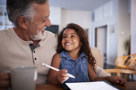 Senior Hispanic man with his granddaughter using tablet computer, looking at each other, close upの写真素材