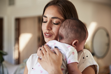 Millennial Hispanic mother with her eyes closed, holding her newborn son to her chest, close upの写真素材