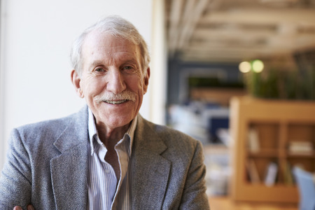 Portrait Of Smiling Senior Businessman In Modern Office Standing By Window