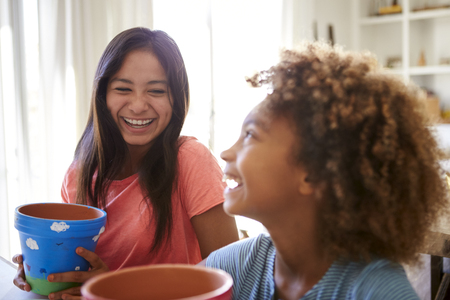 Laughing pre-teen girl and her older girlfriend holding plant pots that theyâve decorated with paints at home, selective focus, close upの写真素材
