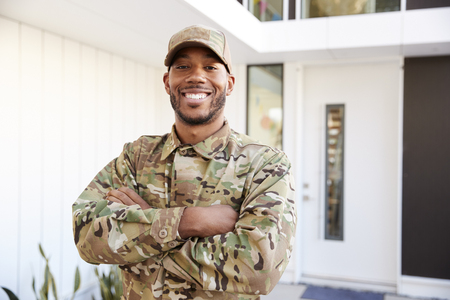 Soldier in camouflage standing outside modern house with arms crossed smiling to camera, close upの写真素材