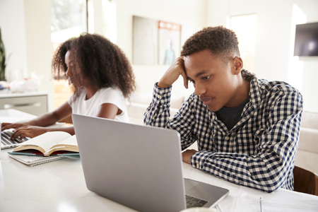 Black teenage brother and sister working on laptop computers at homeの写真素材