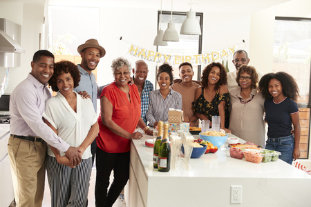 Middle aged black man opening champagne to celebrate at home with his three generation family