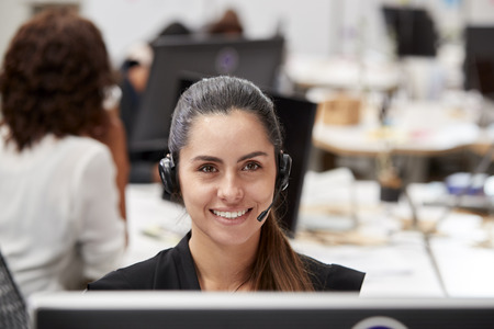 Portrait Of Female Customer Services Agent Working At Desk In Call Center