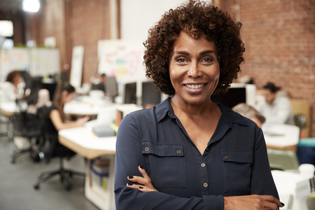 Portrait Of Mature Businesswoman In Open Plan Office With Business Team Working In Backgroundの写真素材