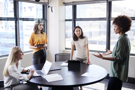 Female creatives in a meeting room listening to their colleague making an informal presentation